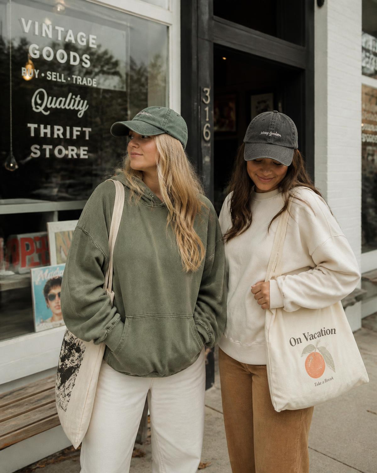 Two women wearing an olive hoodie and cream crewneck with tote bags